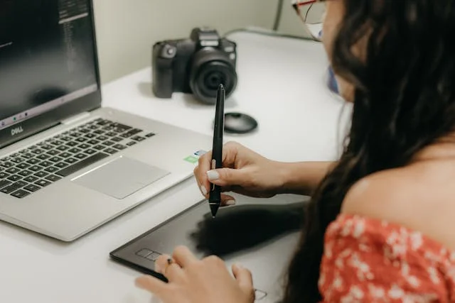Mujer diseñadora y animadora digital que tiene una tableta gráfica en sus manos, junto a una laptop y una cámara fotográfica